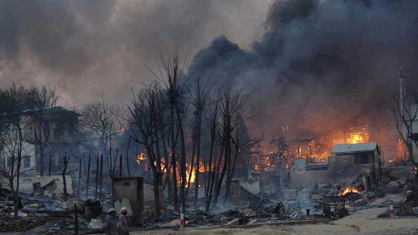 Residents walk past buildings burning in riot-hit Meiktila, central Myanmar