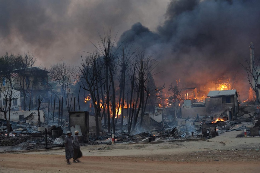 Residents walk past buildings burning in riot-hit Meiktila, central Myanmar