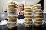 a woman smiles surrounded by two towers of plastic containers containing dinners
