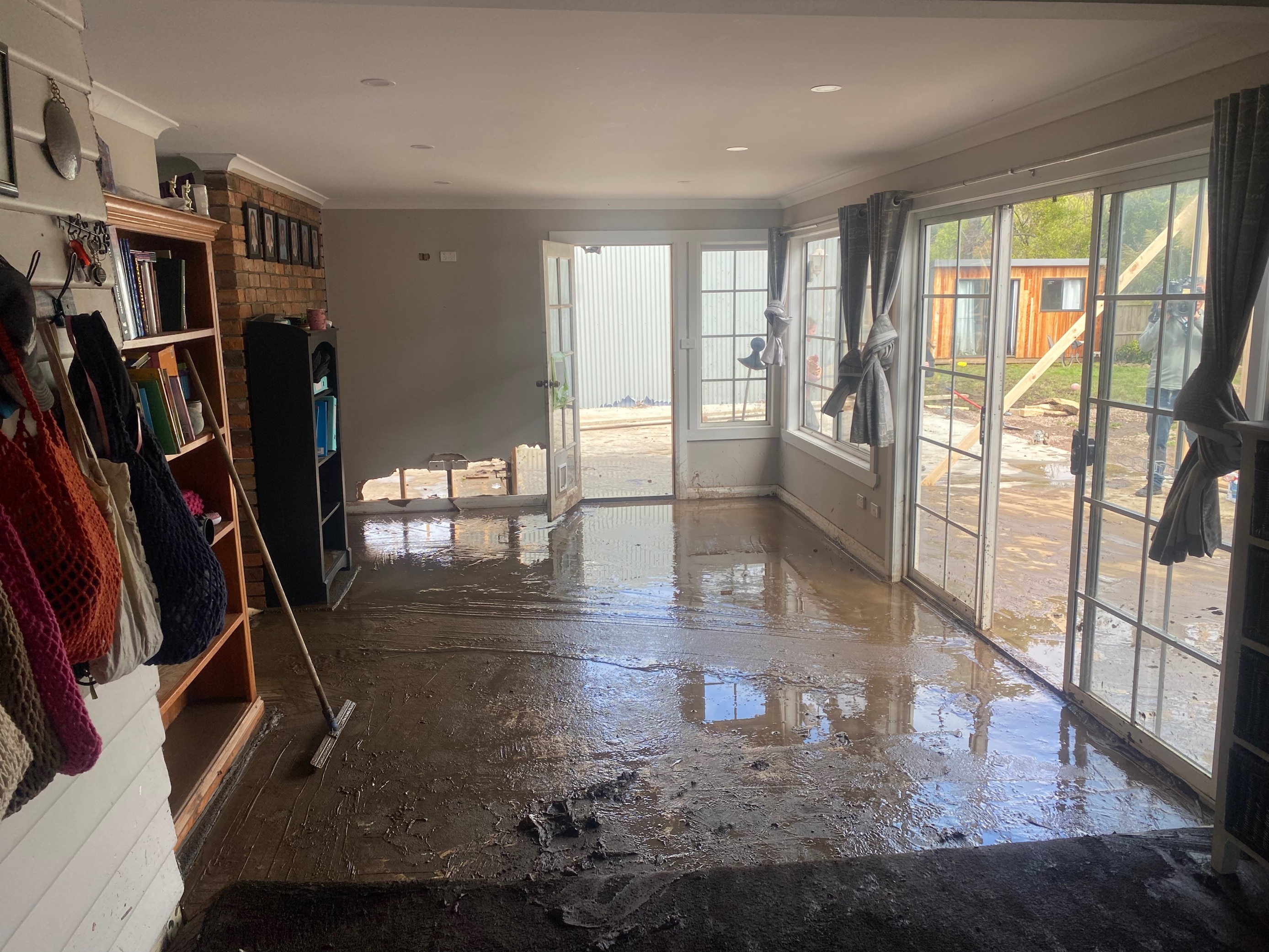 A room is water and mud all over the floor, with a broom leaning up against the wall.