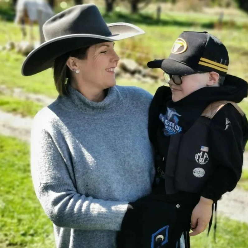 A woman wearing a cowboy hat smiles and holds her son, also wearing a cowboy hat.