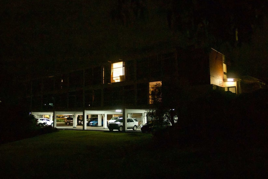 A motel is pictured at night. A light is on in one of the rooms.
