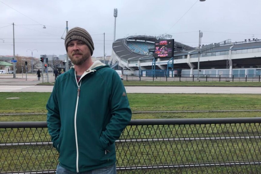 A man wears a beanie pictured in front of a stadium