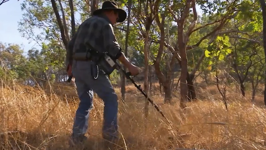 A man uses a metal detector in the outback at sunset.
