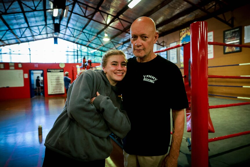 Boxer Marissa Williamson-Pohlman, wrapped in a coat, cuddling into coach Kel Bryant, standing with a stern look