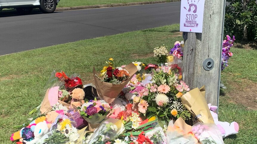 A makeshift memorial of flowers for the Baxter family at Camp Hill, with an anti-domestic violence sign