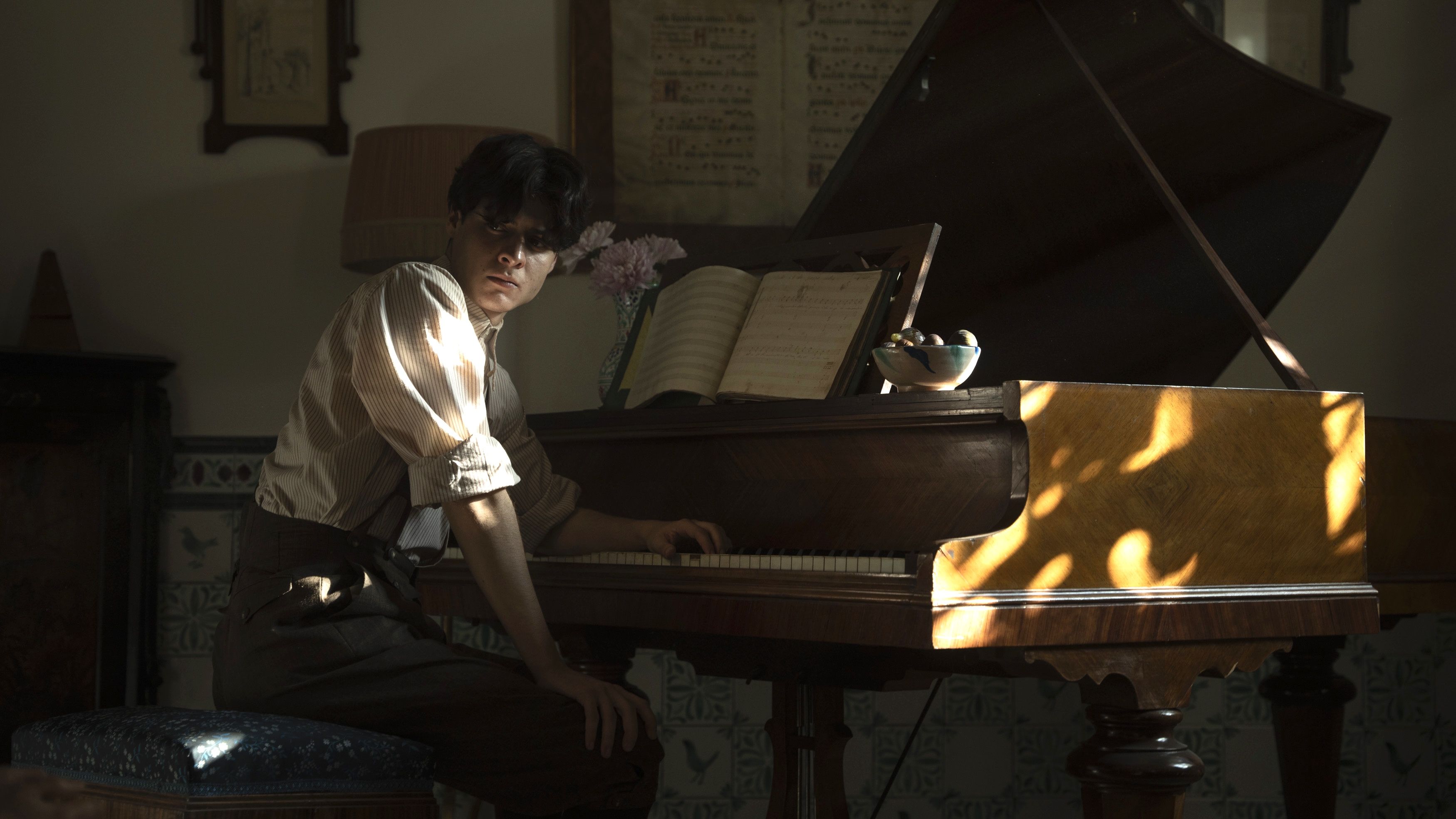 A young man with black hair wearing a white shirt slumps at a piano