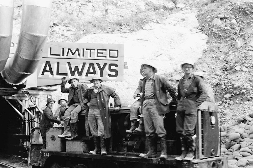 workers sit in a cart on a track outside a tunnel black and white