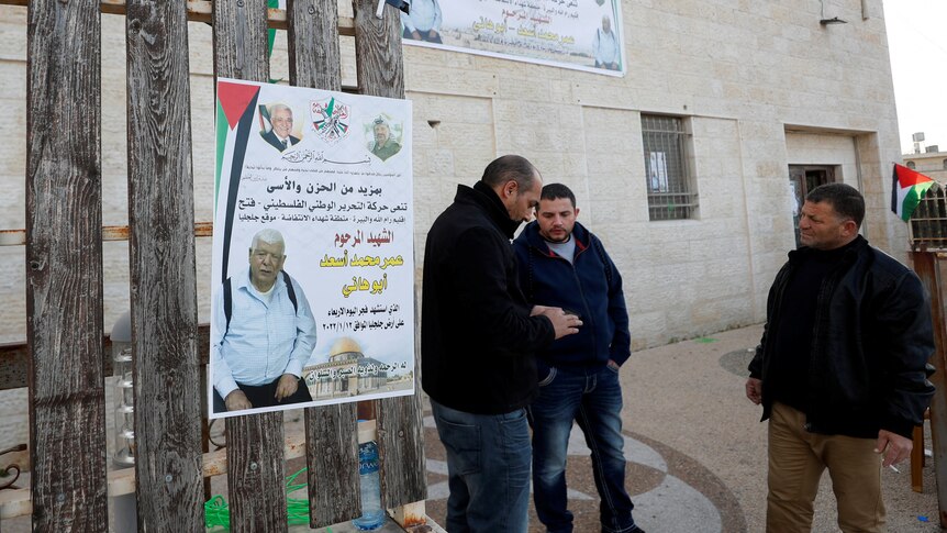 Men mill around a poster of the Palestinian-American killed, January 12, 2022.