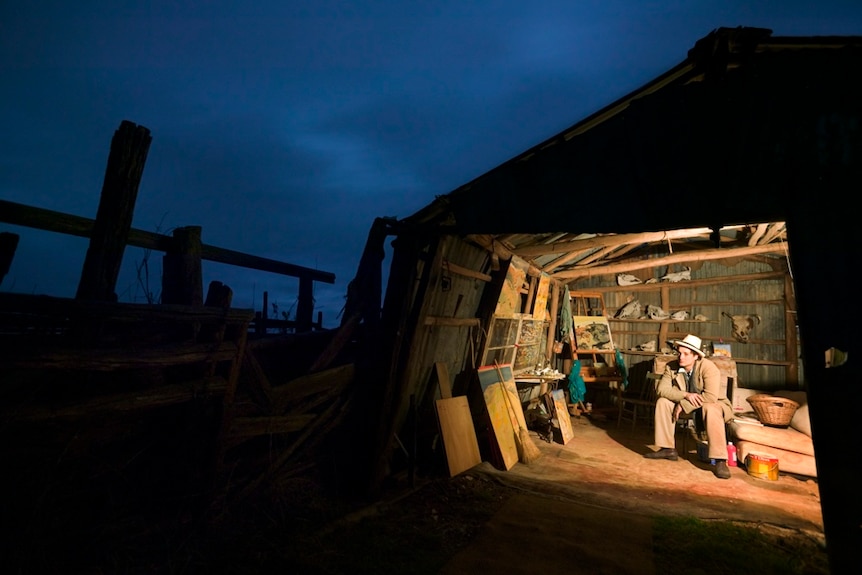 A man sits in a shed looking out at night sky.