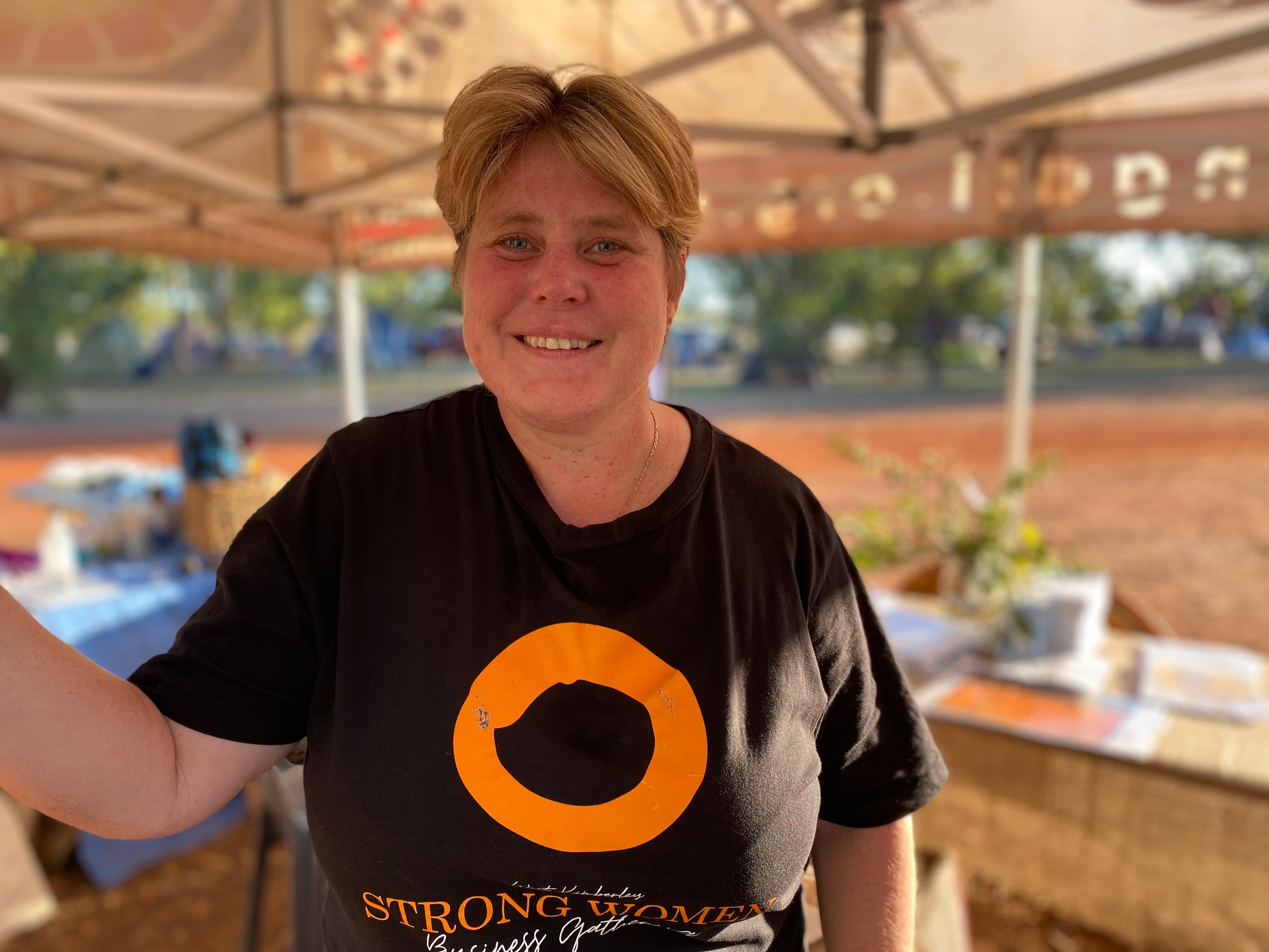 A smiling woman with short blonde hair stands under the event's registration tent