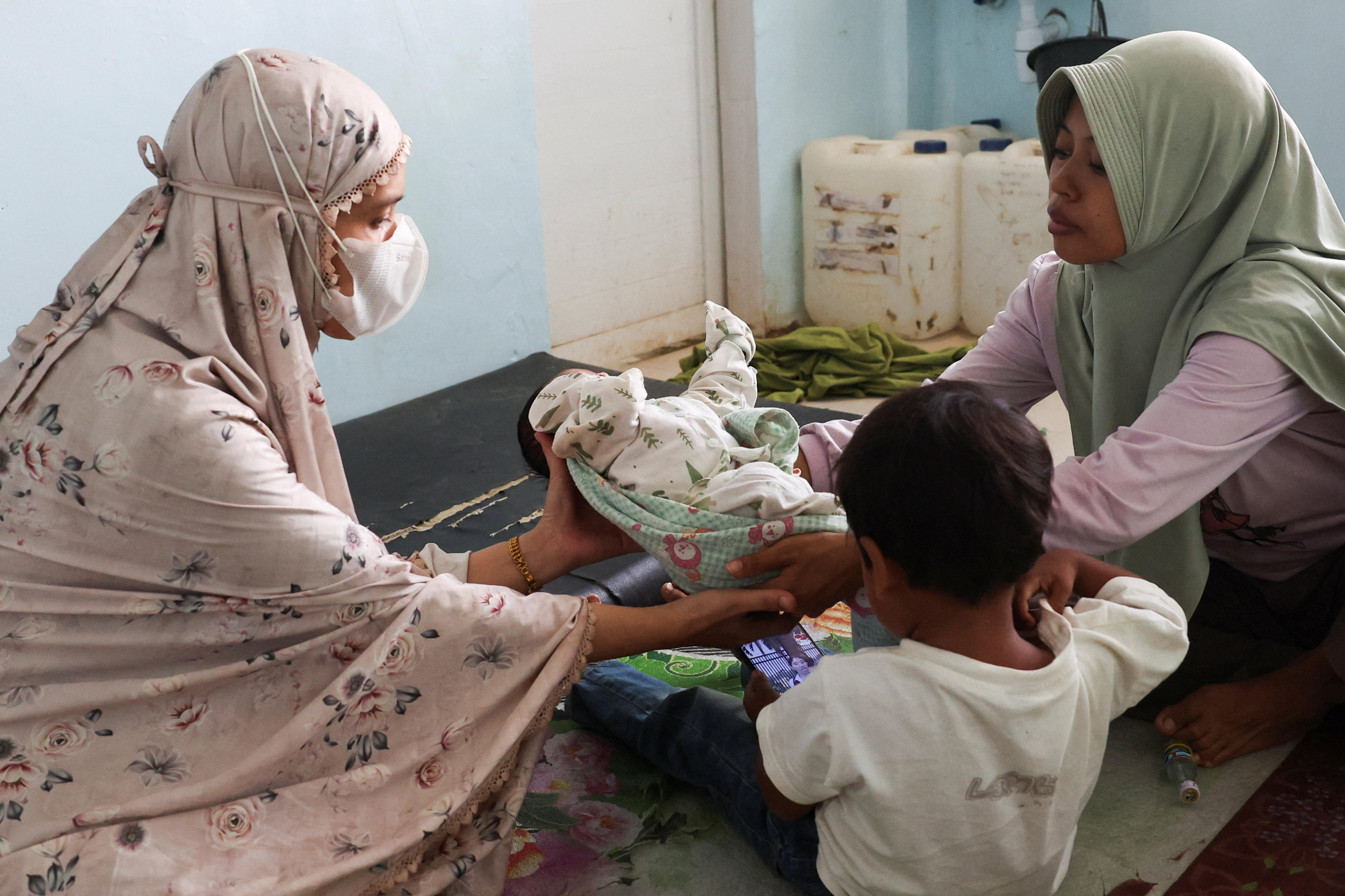 Dos mujeres sostienen a un bebé recién nacido mientras un niño pequeño observa.