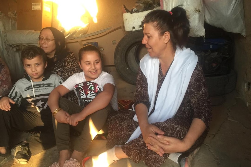 A family sit on the floor of a mud brick home.