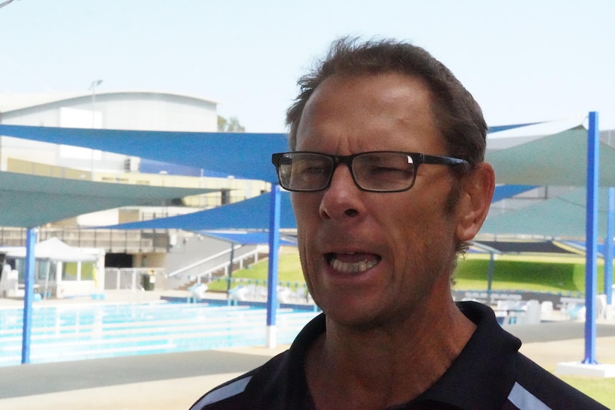 A close up of a man speaking near a swimming pool.