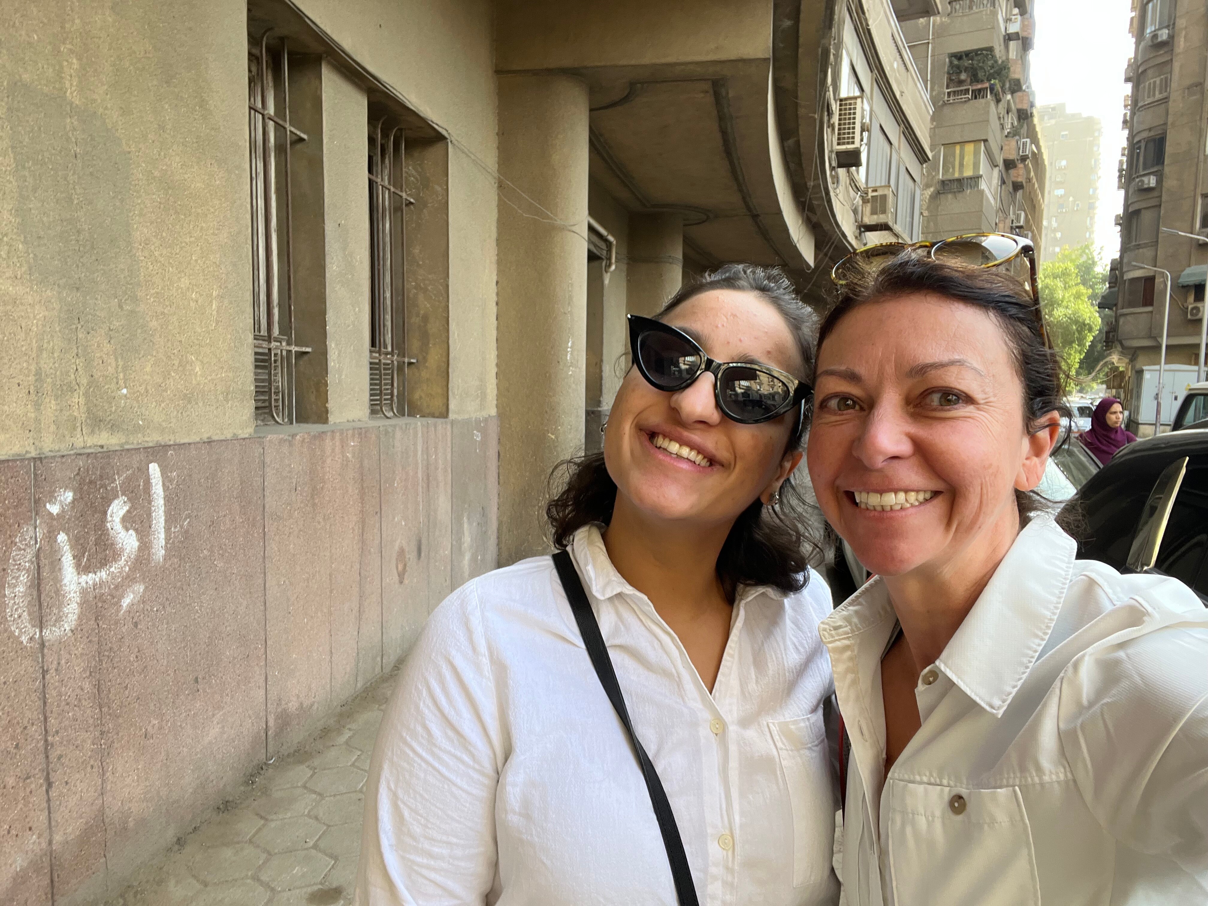 A woman wearing sunglasses smiling with a woman who isn't wearing sunglasses.