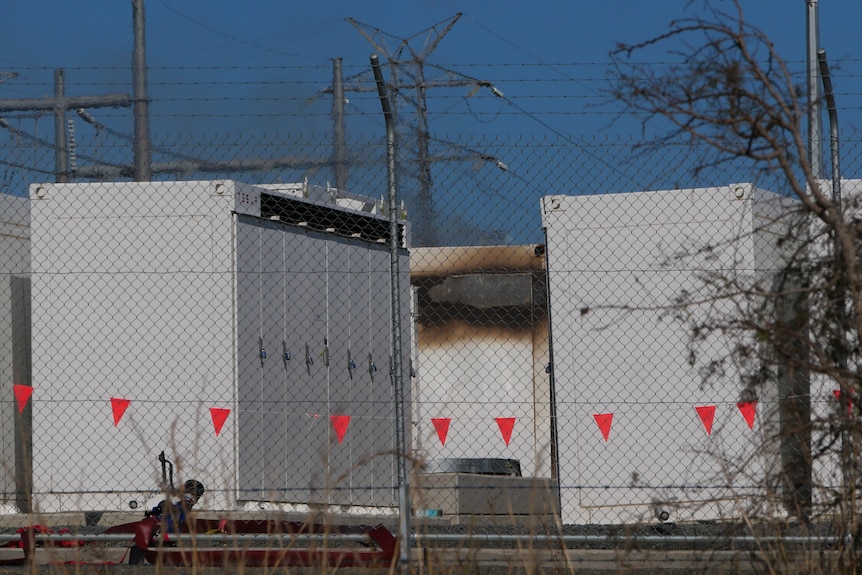 Shipping containers, one of which has been damaged by fire, at an industrial site.