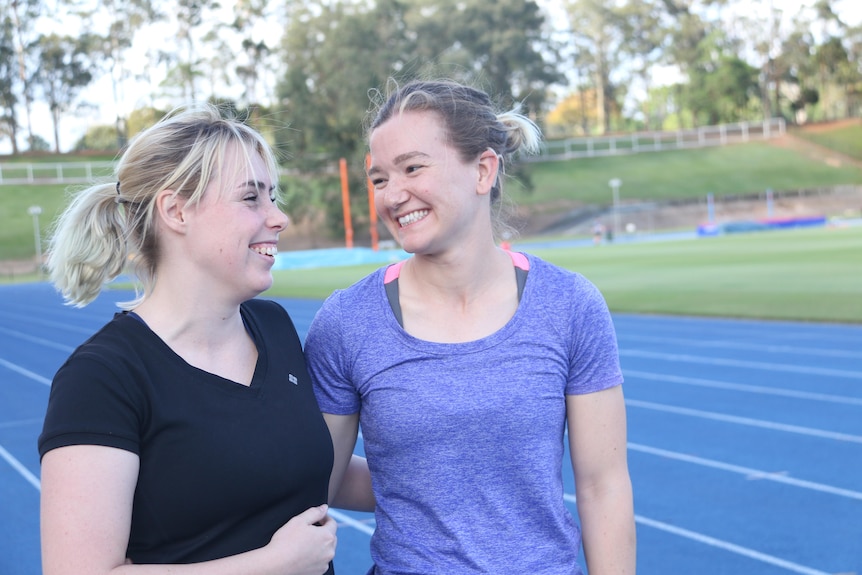 Two women smile at each other on a running track.