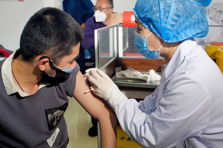 A woman in PPE injects a needle into a man's arm