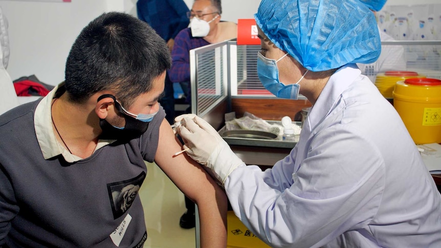 A woman in PPE injects a needle into a man's arm