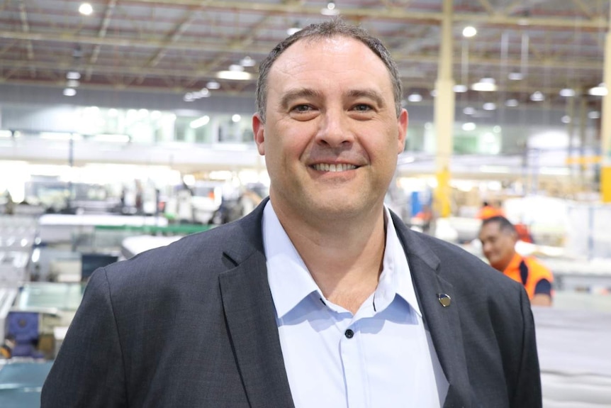 A man wearing a business suit, standing inside a mattress factory.