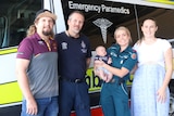 A group of four people in front of an ambulance, holding a baby. 