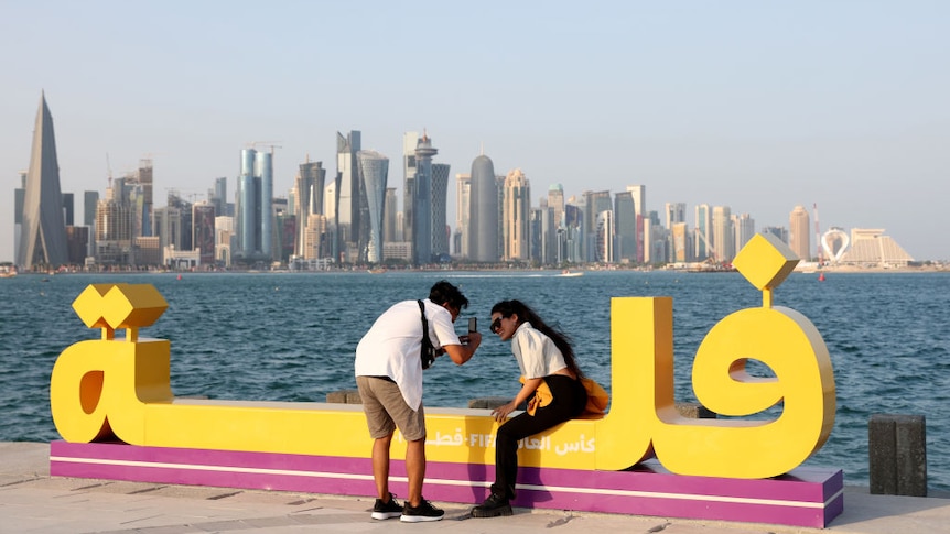 A man and woman take a selfie with Doha city in the background across the water
