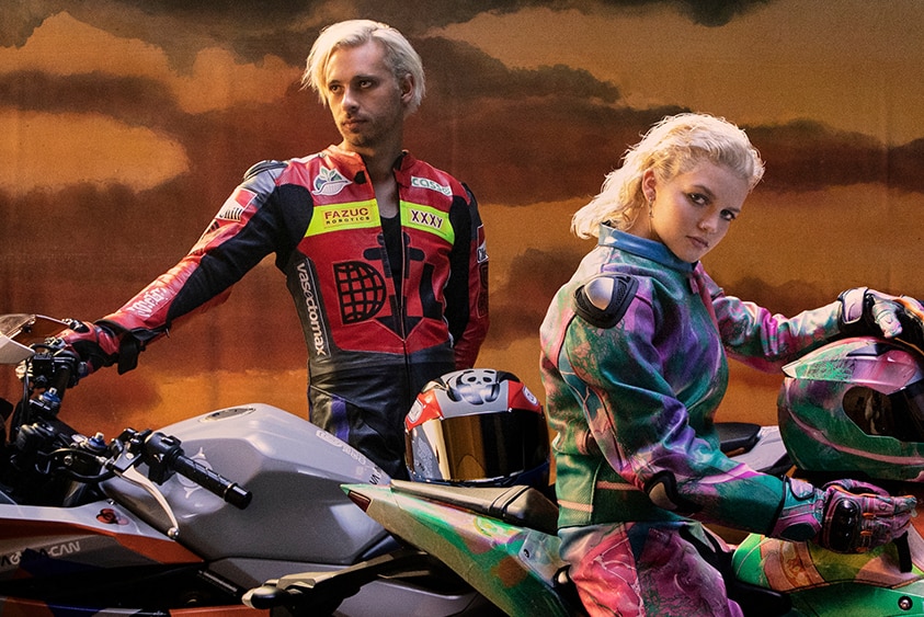 A 2022 press shot Flume and MAY-A posing on motorcycles with sportswear jackets
