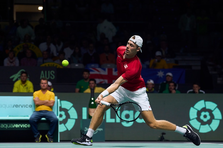 Denis Shapovalov plays a forehand as Leyton Hewitt looks on