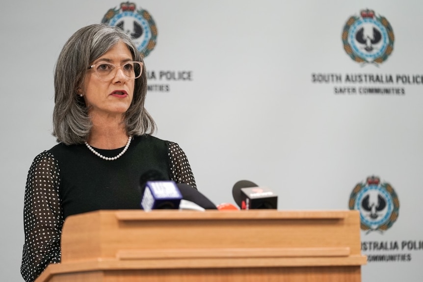 Nicola Spurrier stands at a podium with microphones in front of her