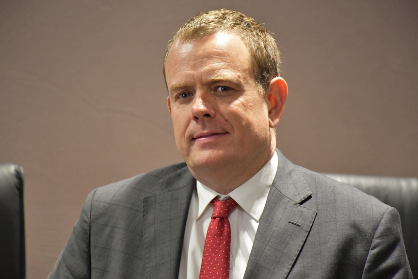 A man with short brown hair and a red tie smiles at the camera.