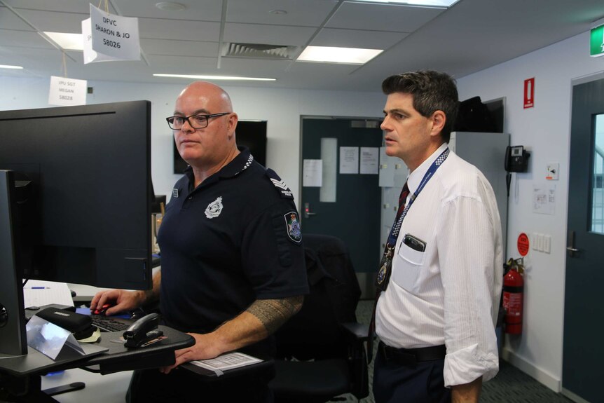 Two male police officers look at a computer screen in an office.