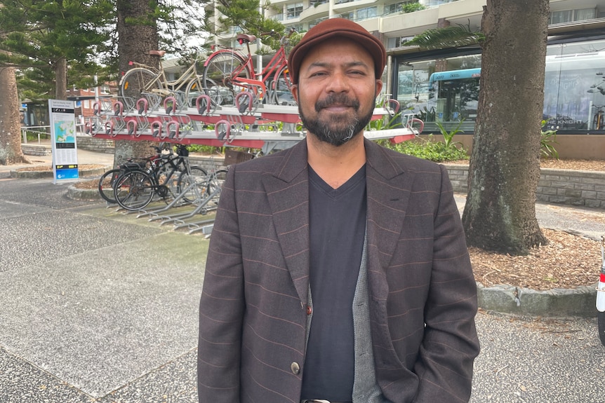 A man in a hat with a beard stands in front of a rack of bicycles.