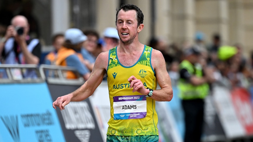 Marathon runner Liam Adams, wearing green and gold, crosses the finish line.