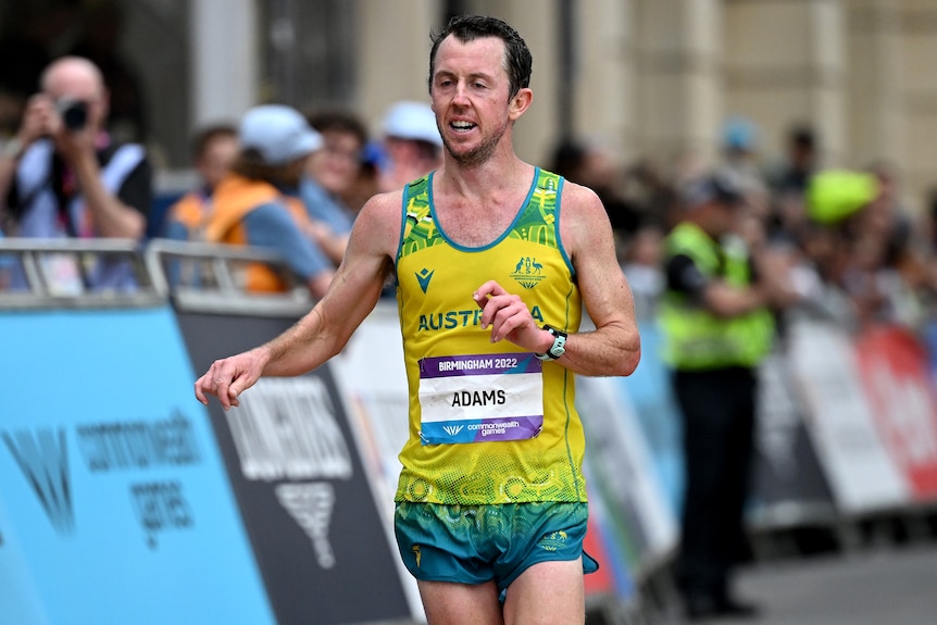 Marathon runner Liam Adams, wearing green and gold, crosses the finish line.