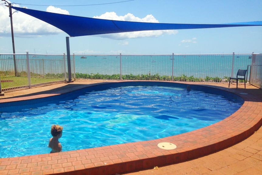 A child swims in a pool in a courtyard with a view of the ocean.