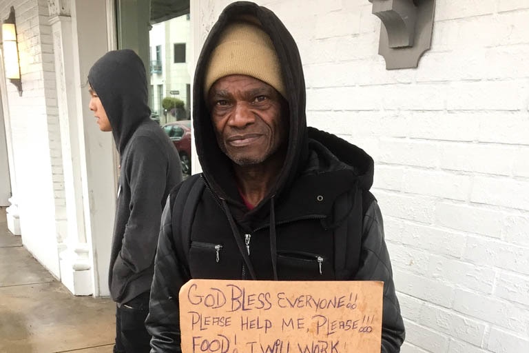 Man holds a sign asking for food and work in LA