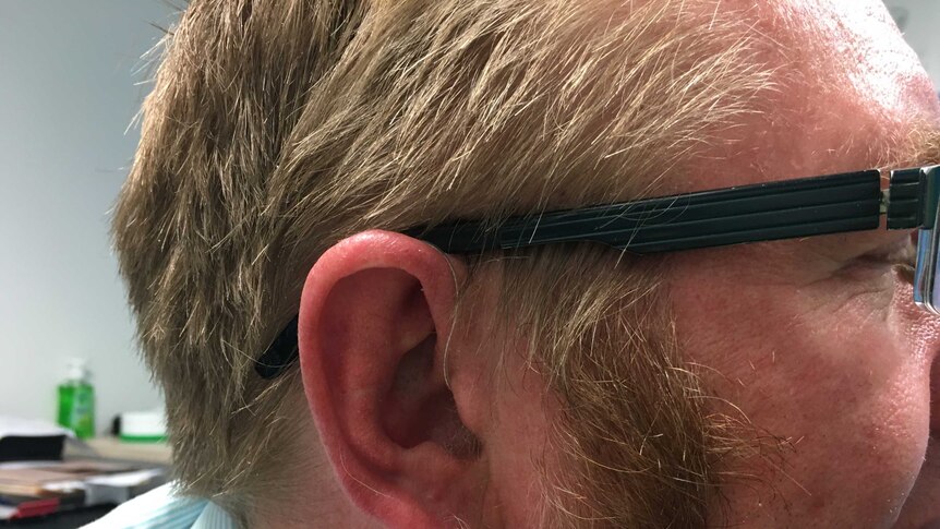 side on pic of a man wearing glasses and an almost invisible hearing aid