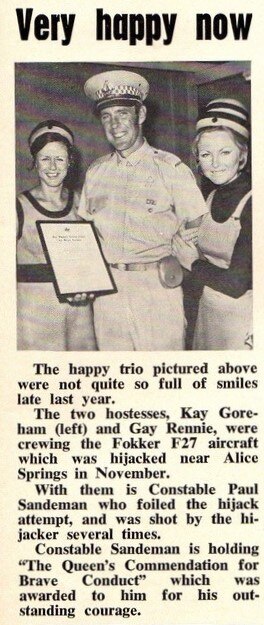 A newspaper clipping of a police holding an award, with an air hostess on each side of him,