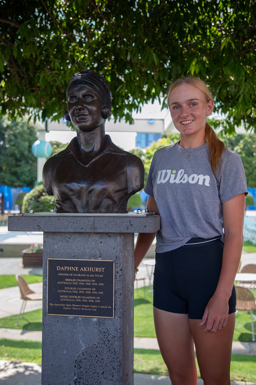 Taylah Preston stands next to a bronze statue of Daphne Akhurst. Preston looks at the camera and smiles.