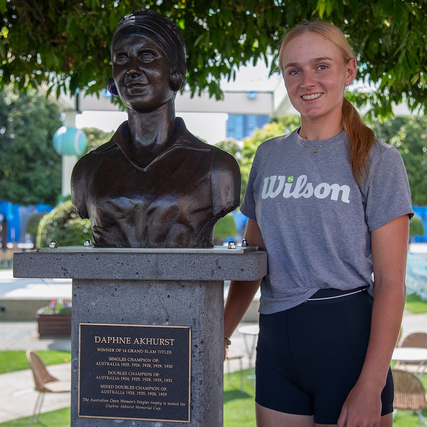 Taylah Preston stands next to a bronze statue of Daphne Akhurst. Preston is looking at the camera, smiling.