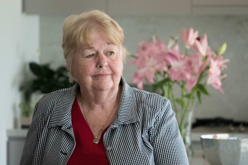 A woman in a checked shirt with pink flowers in the background.