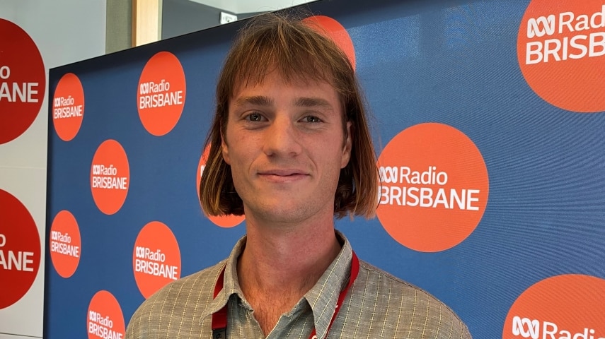 Joel Ward smiles in front of an ABC Radio Brisbane wall.