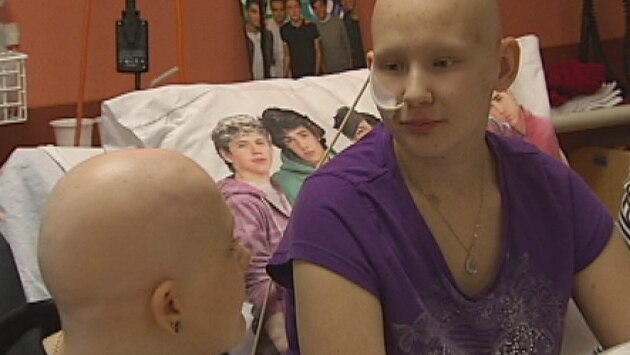 Head and shoulder photo of two young female cancer patients sitting in hospital bed with one direction poster and pillow in background - 22 August 2013