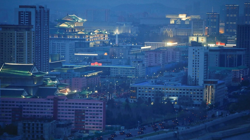 Military drive trucks through Pyongyang at night, set against the city skyline