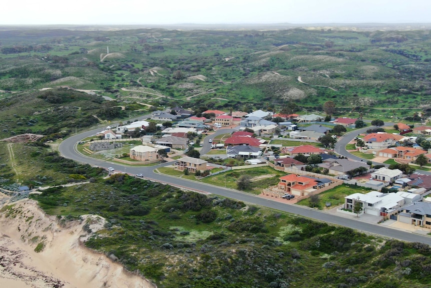 A suburban neighbourhood butts on to the coast, with lush green highlands in the background