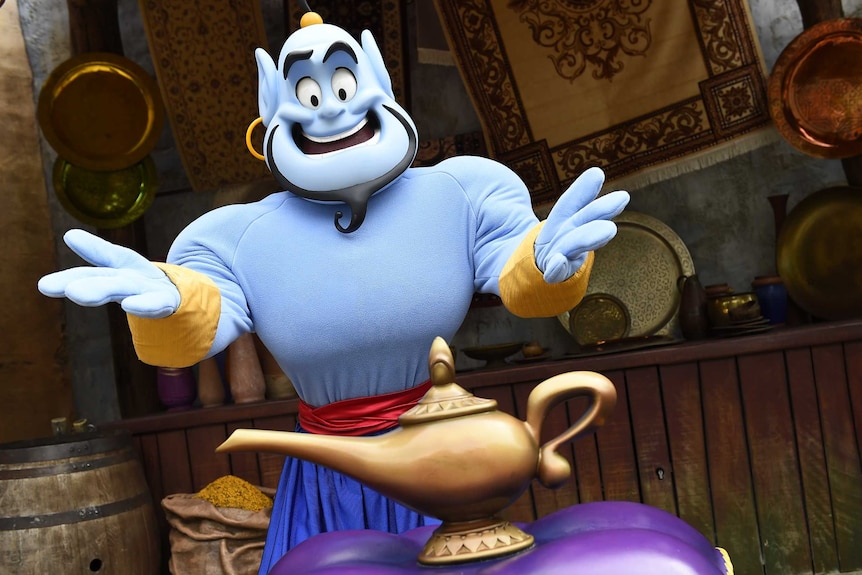 Aladdin's Genie in costume presents a lamp on a cushion.