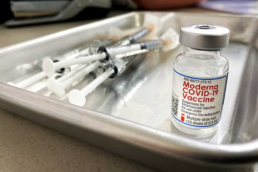 A vial of the Moderna vaccine next to a pile of syringes