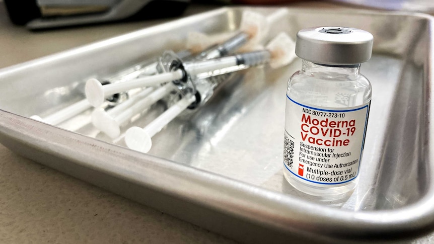 A vial of the Moderna vaccine next to a pile of syringes