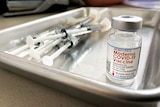 A vial of the Moderna vaccine next to a pile of syringes