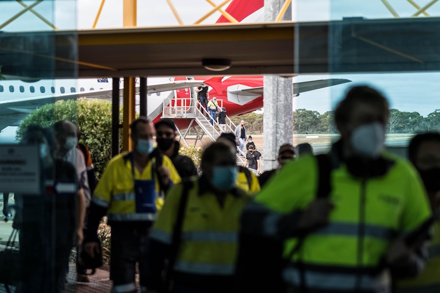 Des gens entrent dans l'aéroport après être arrivés à bord d'un jet Qantas.  